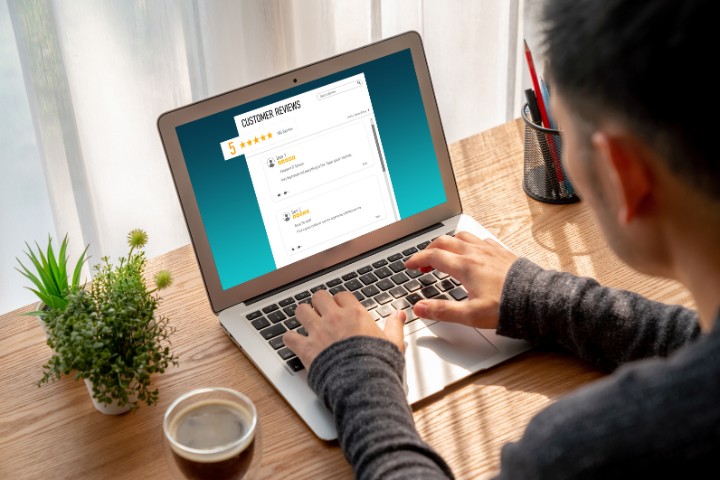 A person reviewing feedback on a laptop, with customer reviews visible on the screen, alongside a coffee cup and a plant for a cozy work environment