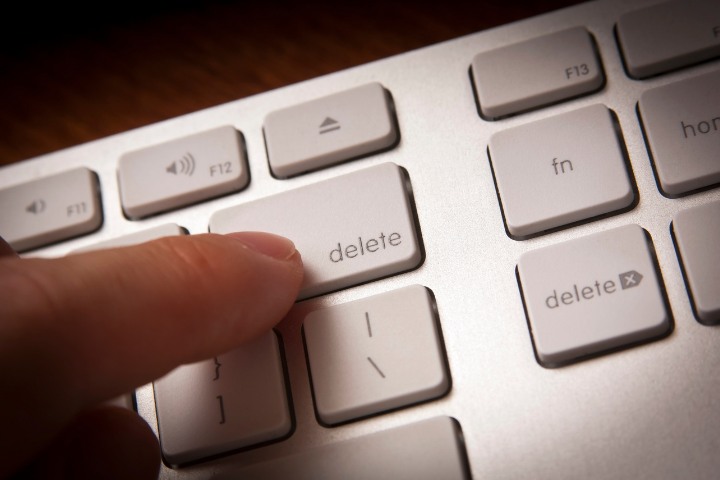 A close-up view of a person's finger pressing the 'delete' key on a silver computer keyboard